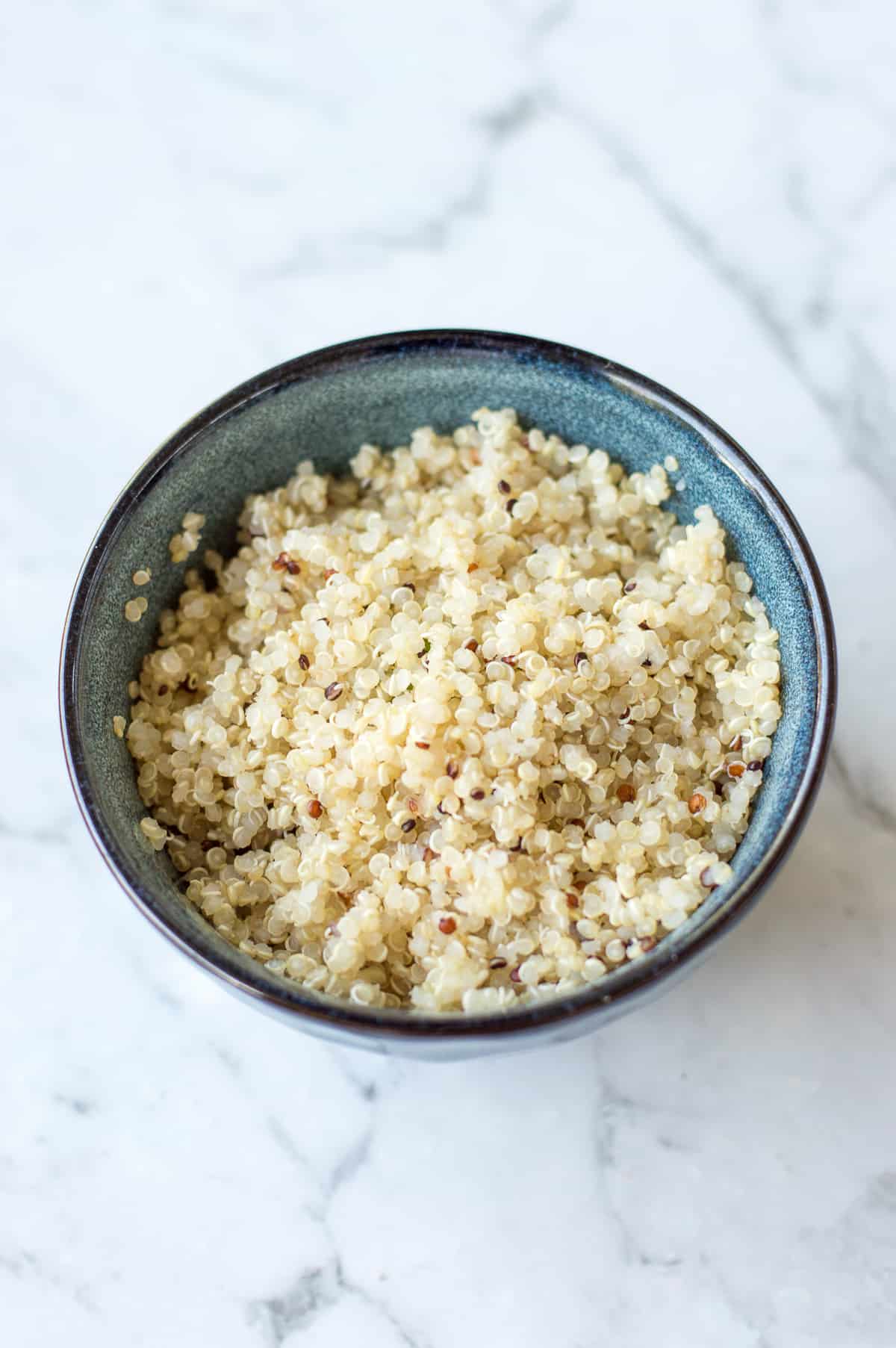 cooked quinoa in blue bowl on white marble background