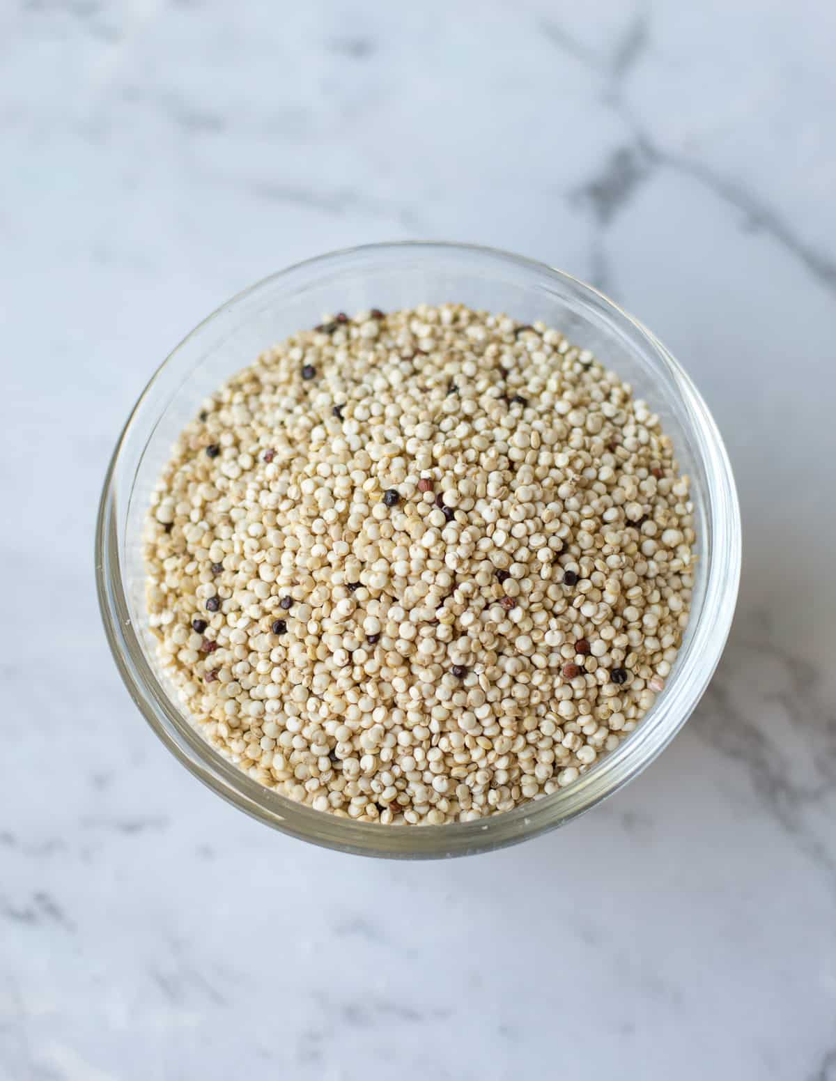 uncooked quinoa in glass bowl on white marble background