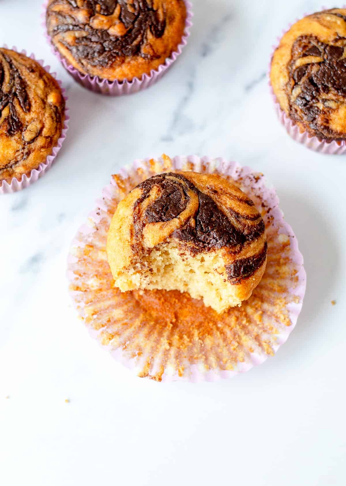 Nutella swirl muffins with a bite taken out. sitting on a marble benchtop.