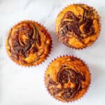3 Muffins with a Swirl of Nutella on top, sitting on a white marble benchtop.