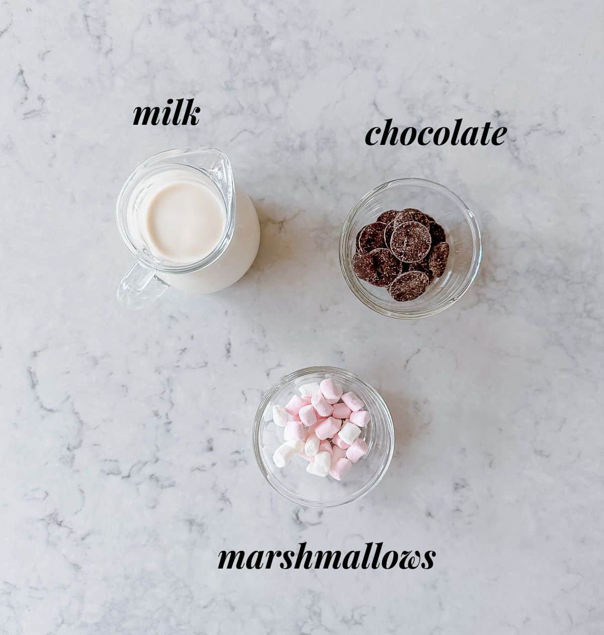 Milk, chocolate and marshmallows sitting on a marble benchtop.