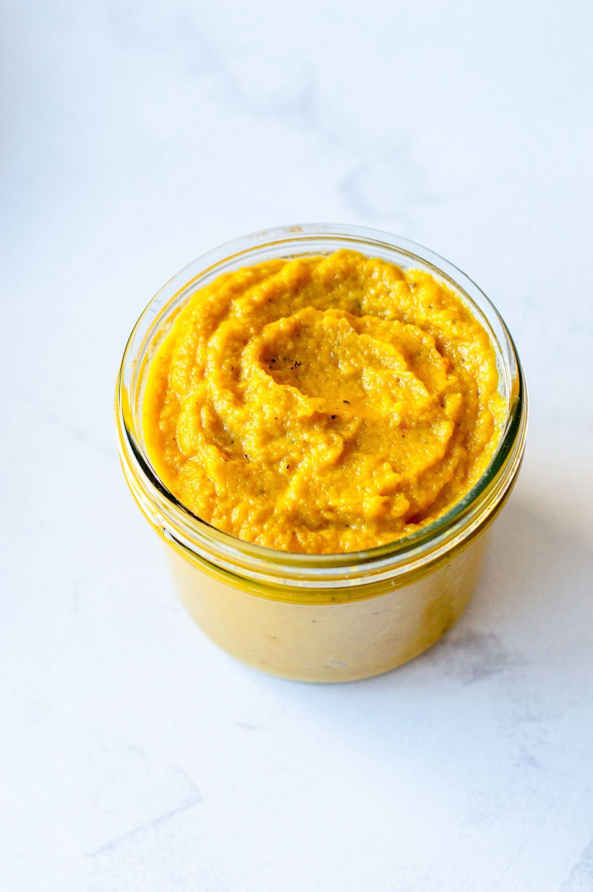 A glass jar filled with vegetable stock concentrate. Sitting on a marble benchtop.