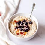 Porridge in a white bowl with blueberries and maple syrup.