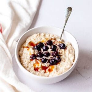Porridge in a white bowl with blueberries and maple syrup.