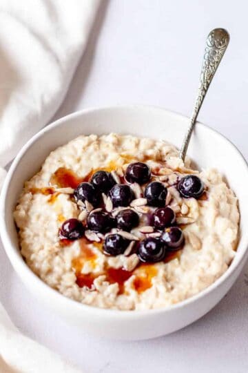 Porridge in a white bowl with blueberries and maple syrup.