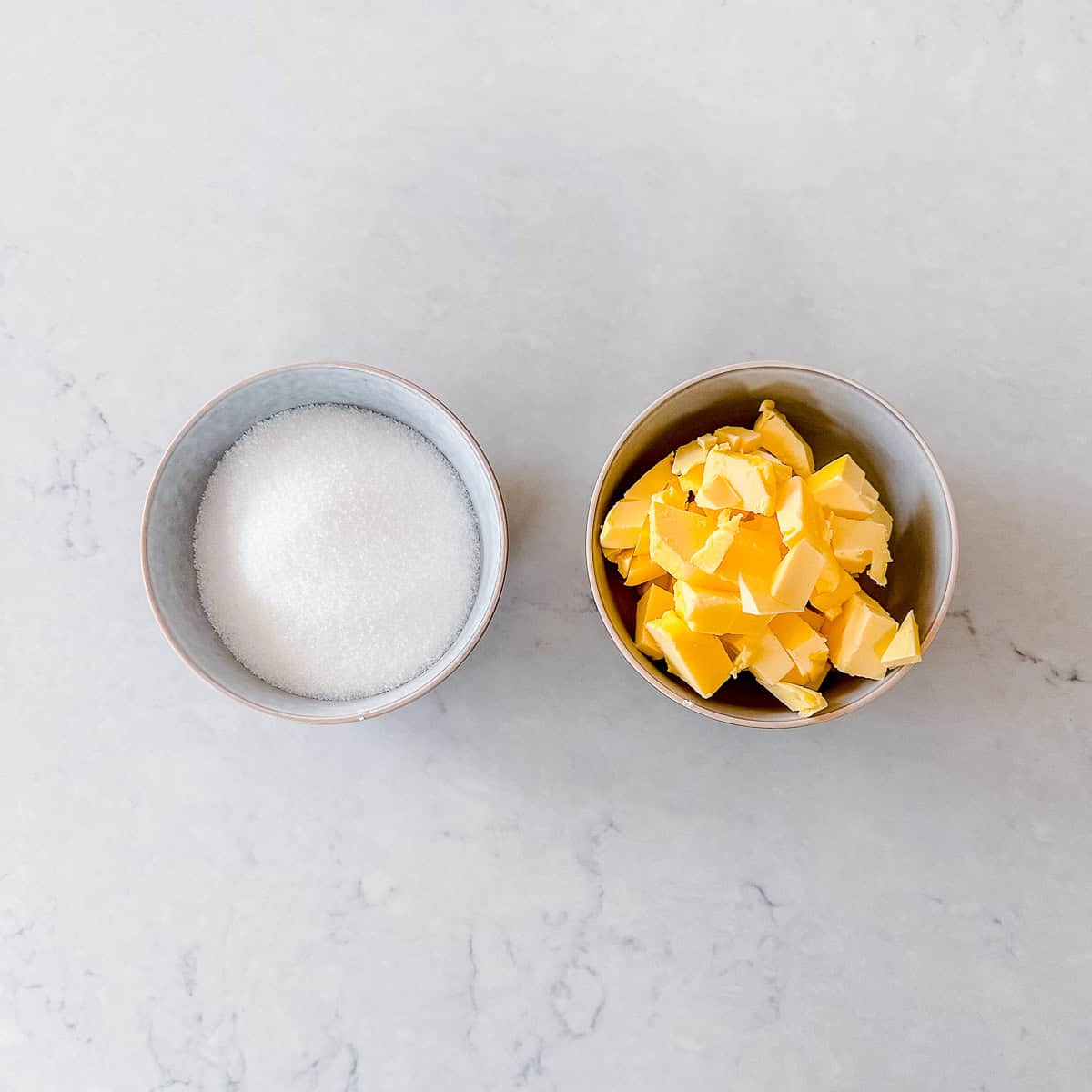 A bowl of butter and sugar sitting side by side on a marble benchtop.