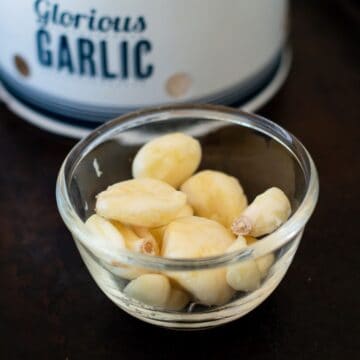 raw peeled garlic in a glass bowl.