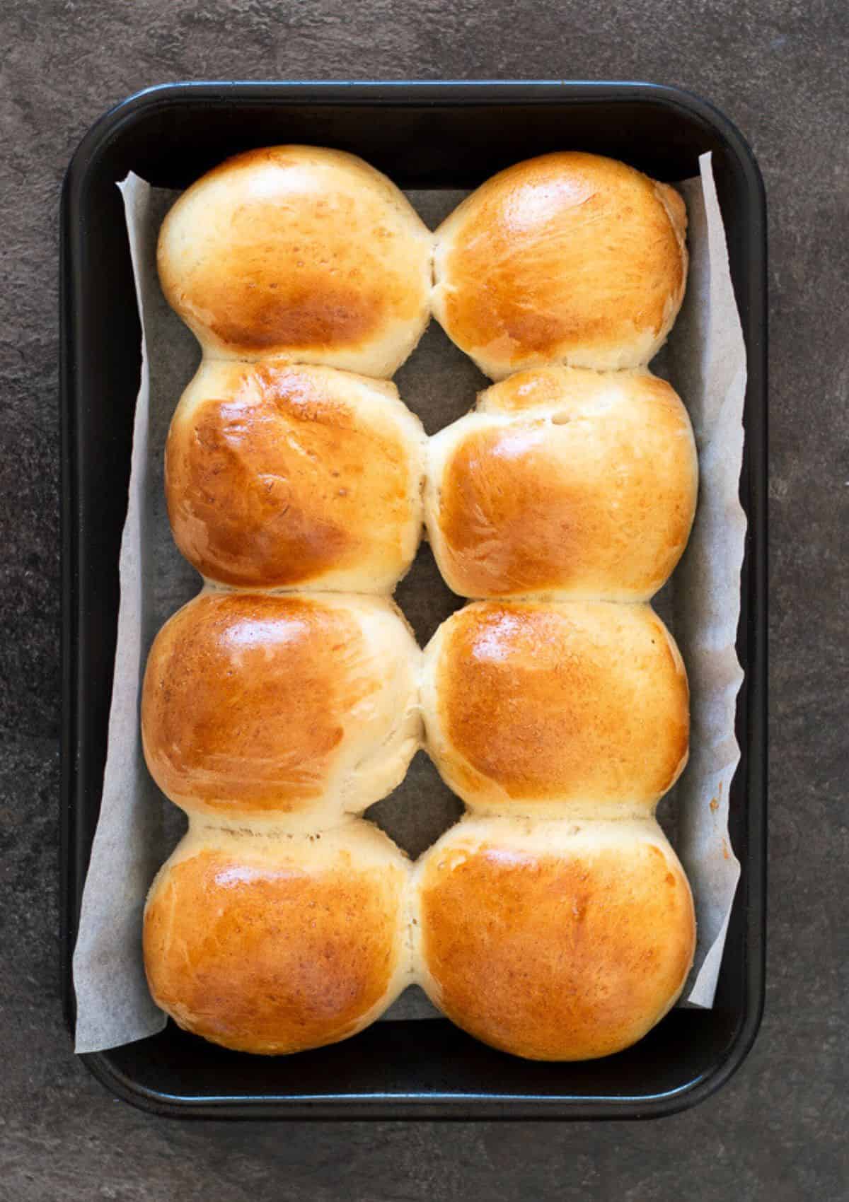 8 white bread rolls on a baking tray.