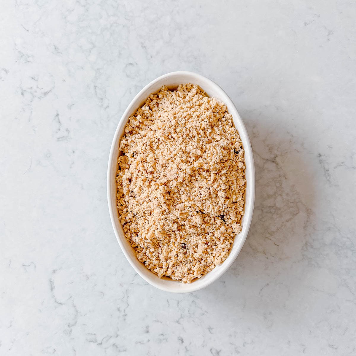 Unbaked rhubarb crumble in an oval dish.