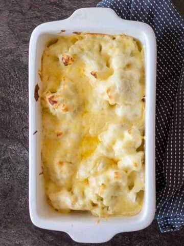 cauliflower cheese in a white baking dish on a dark background.