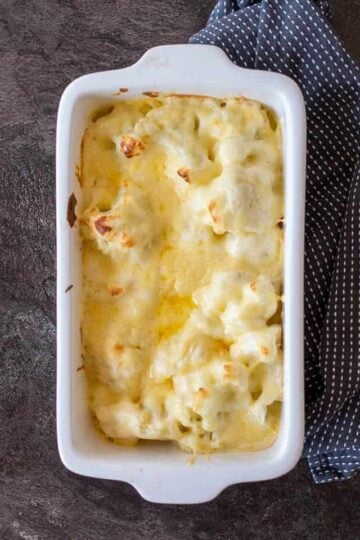 cauliflower cheese in a white baking dish on a dark background.