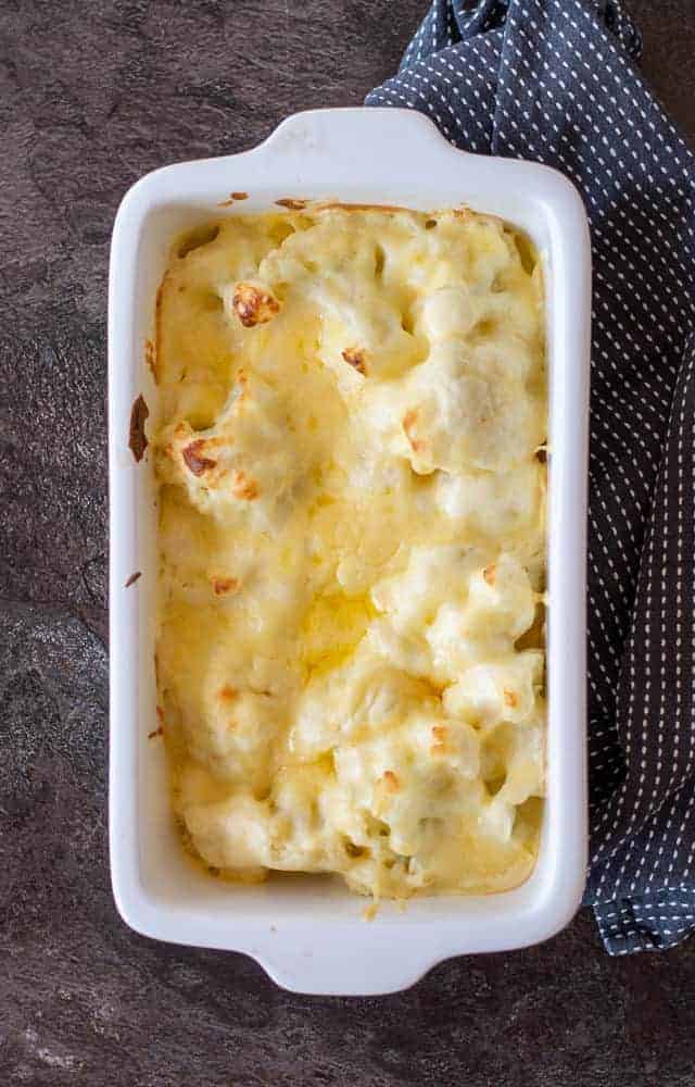 cauliflower cheese in a white baking dish on a dark background.