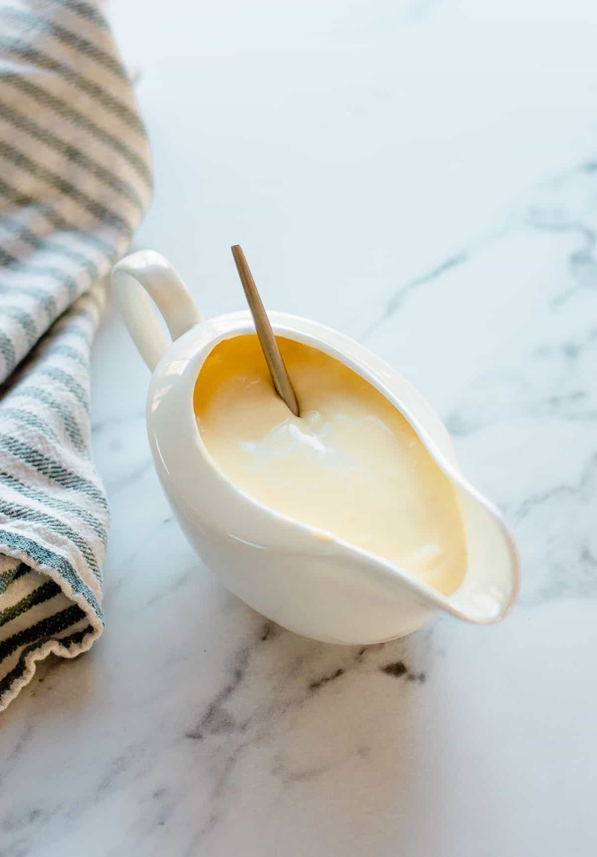 Cheese sauce in a white jug sitting next to a blue and white striped tea towel.