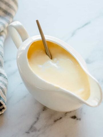 Cheese sauce in a white jug with striped tea towel.