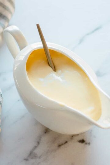 Cheese sauce in a white jug with striped tea towel.