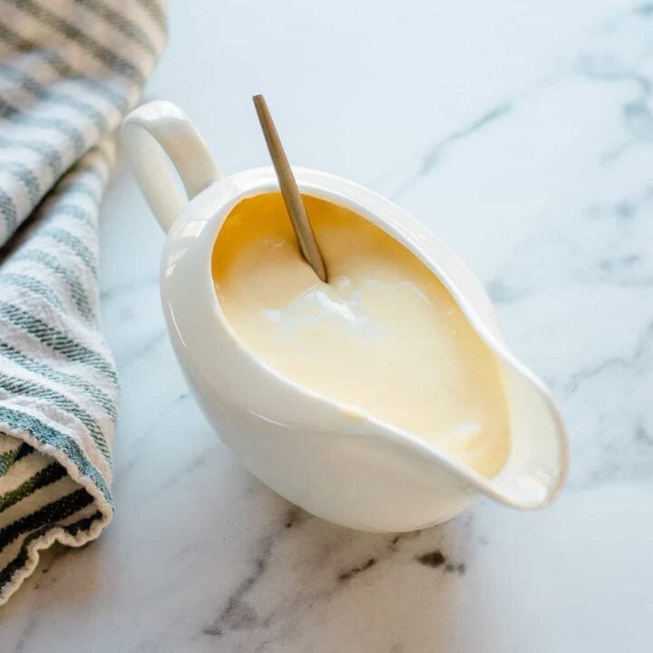 Cheese sauce in a white jug with striped tea towel.