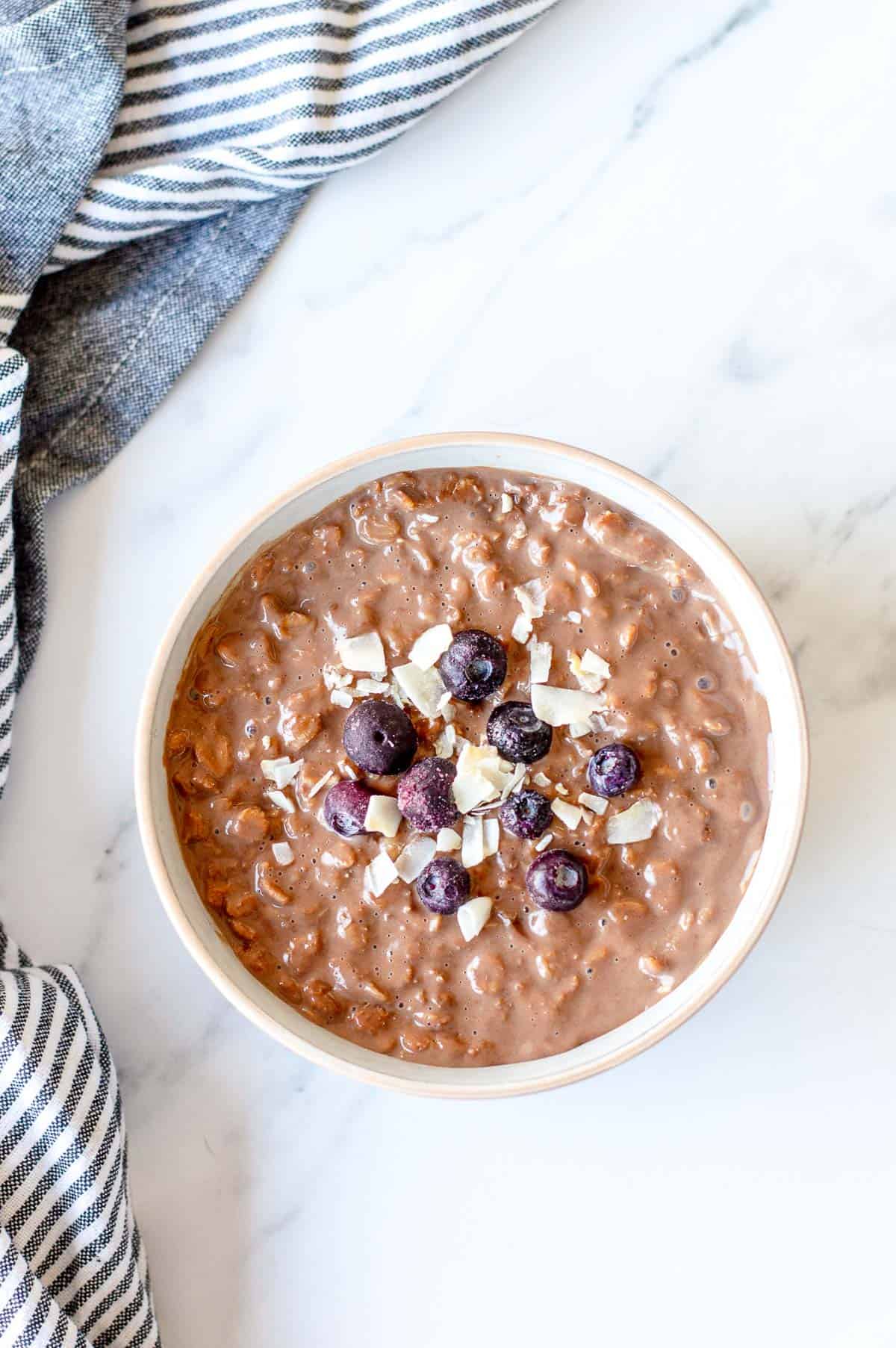 Chocolate Porridge with blueberries and coconut chips in a white bowl.