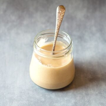 Homemade Tahini in a glass jar with spoon.