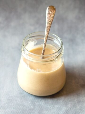 Homemade Tahini in a glass jar with spoon.