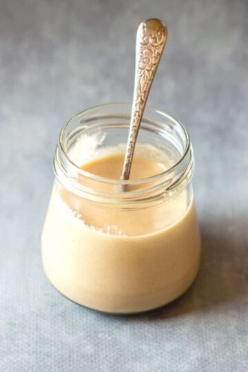 Homemade Tahini in a glass jar with spoon.