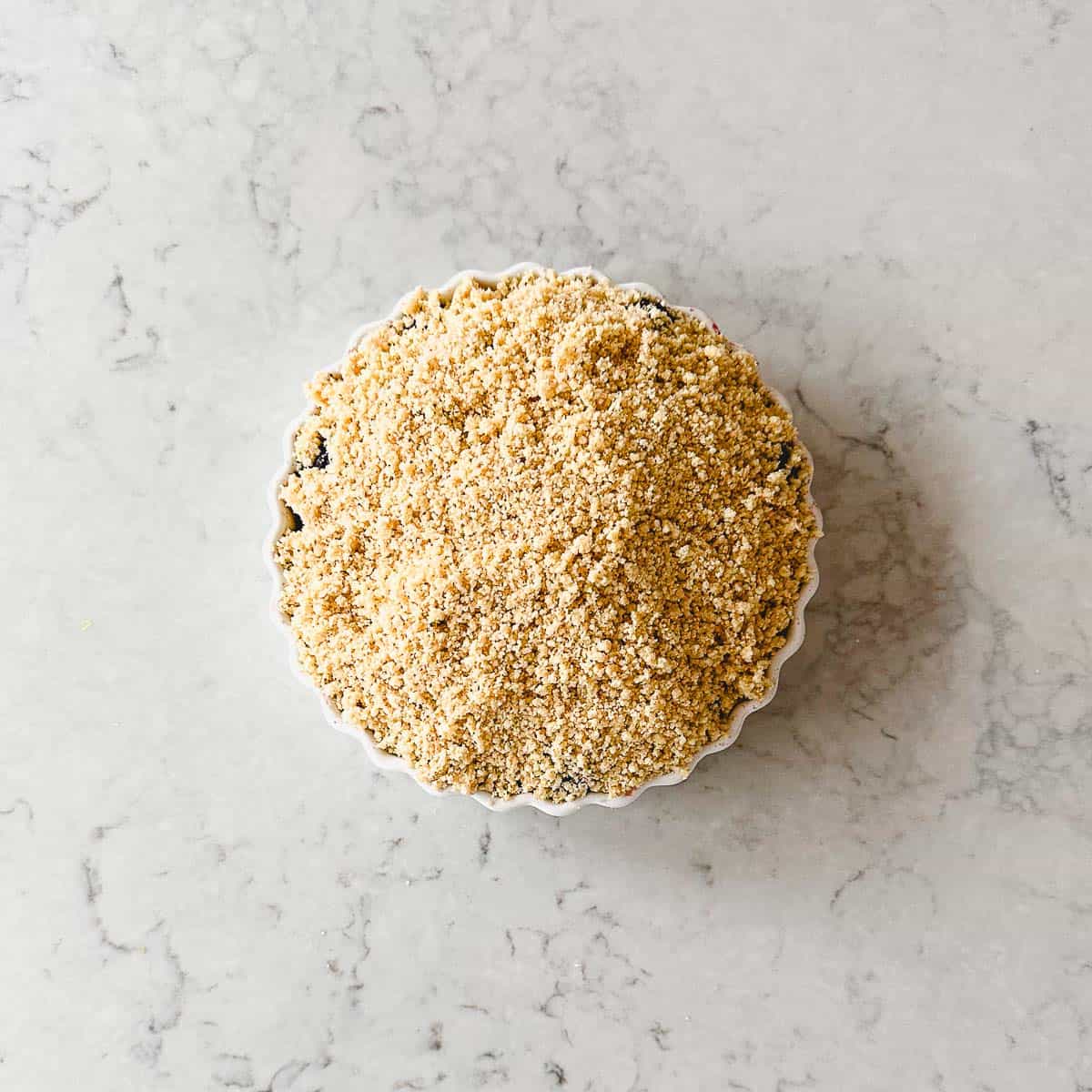 A small round dish filled with a crumbly, golden-brown mixture sits on a light, marbled worktop.