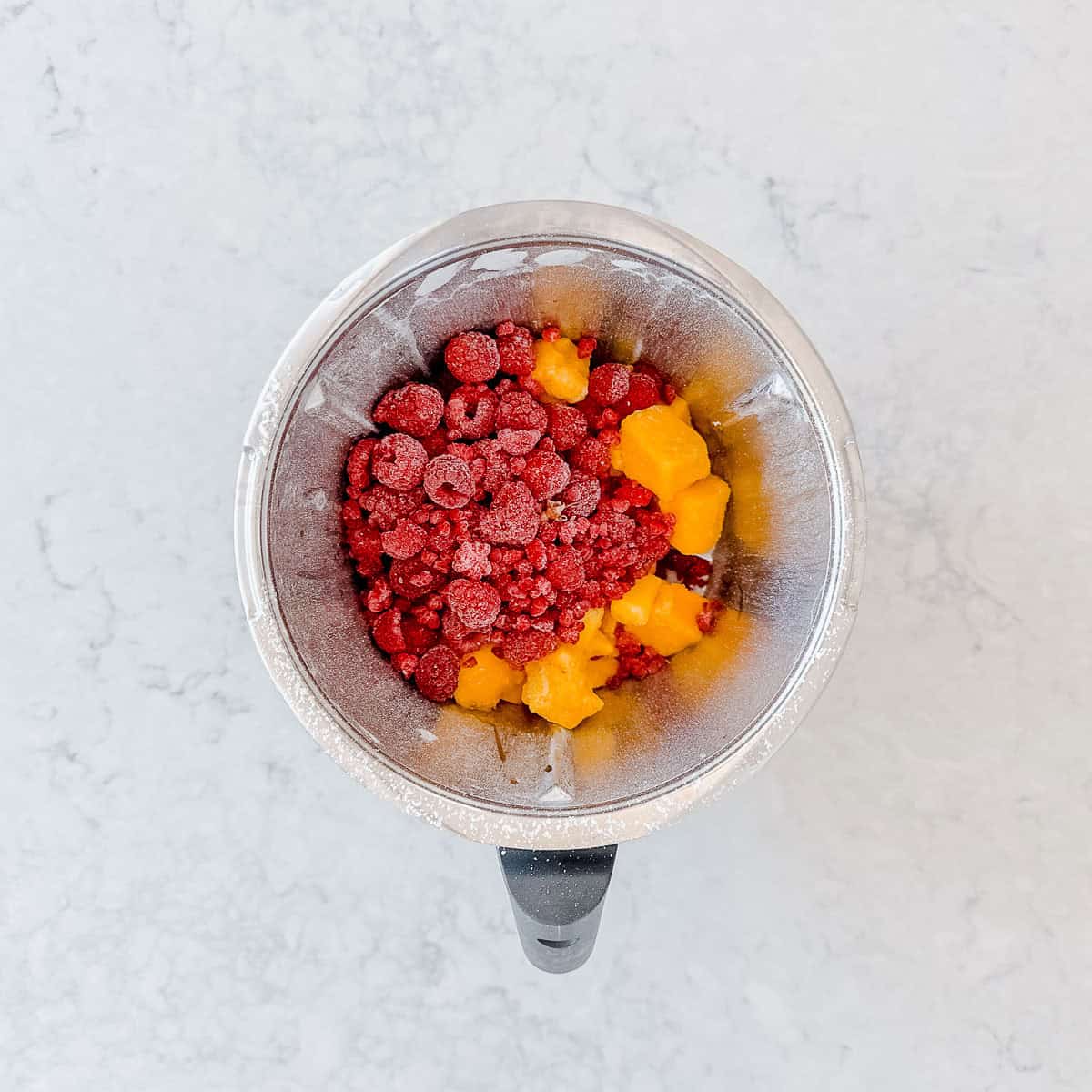 Frozen Raspberries and Mango in a Thermomix bowl.