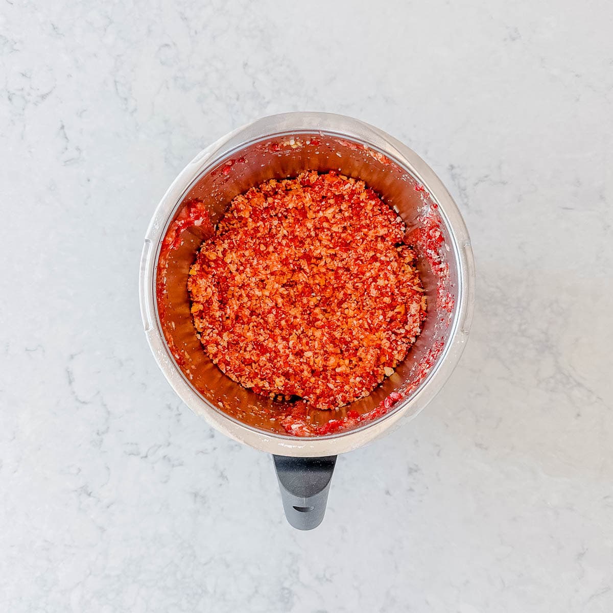 Chopped up frozen mangoes and raspberries in a Thermomix bowl.