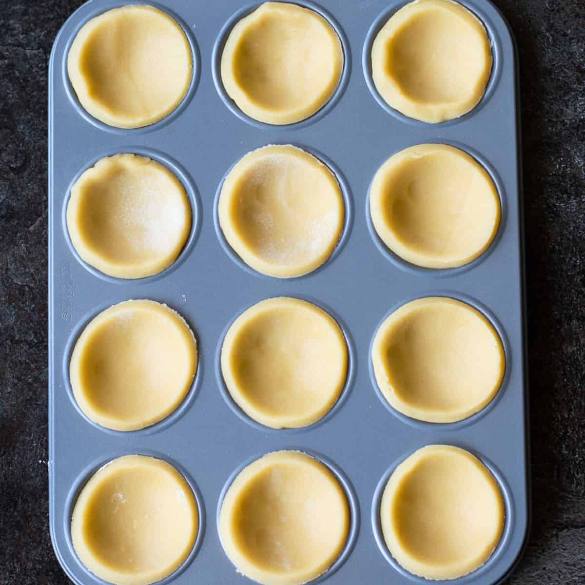 Raw pastry rounds in a grey patty tin.