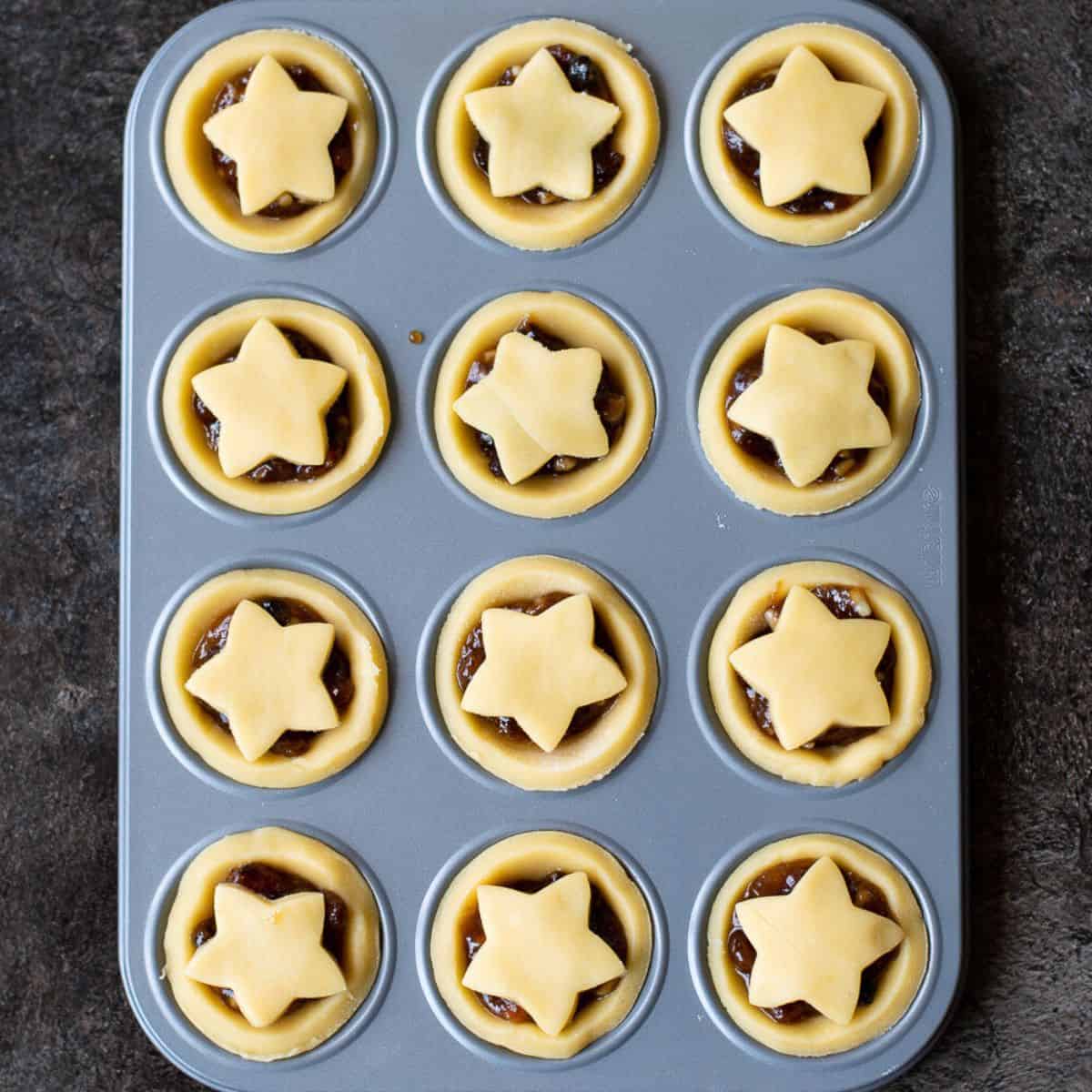raw mince pies with stars on them in a patty tin waiting to be baked