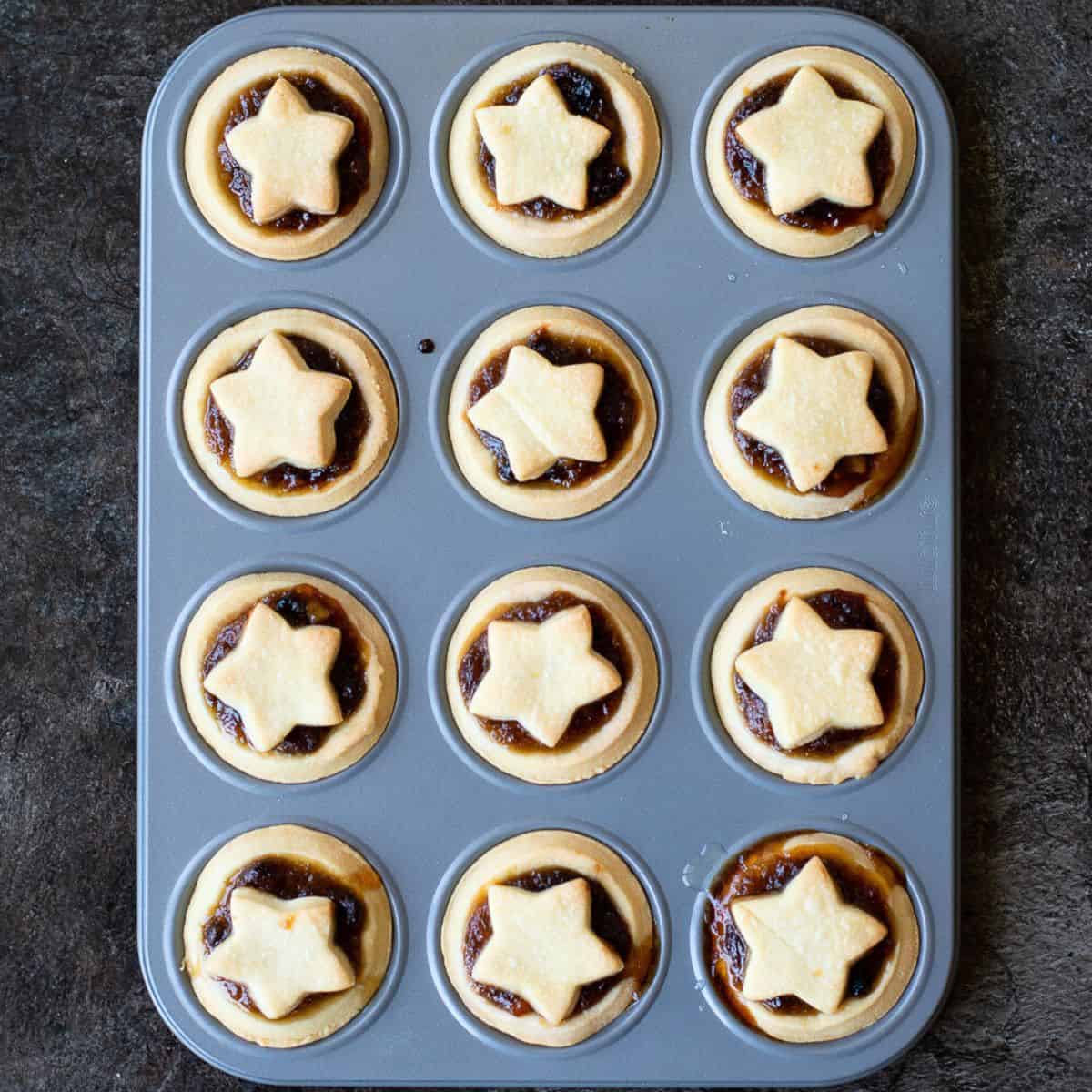 mince pies with stars on them in a grey patty tin.