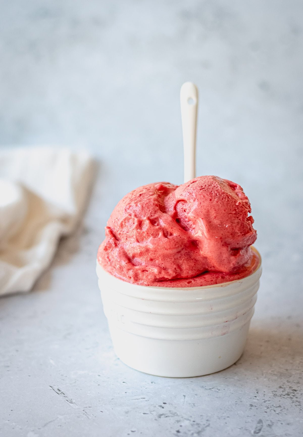 Raspberry mango sorbet in a white ramekin on a grey background.