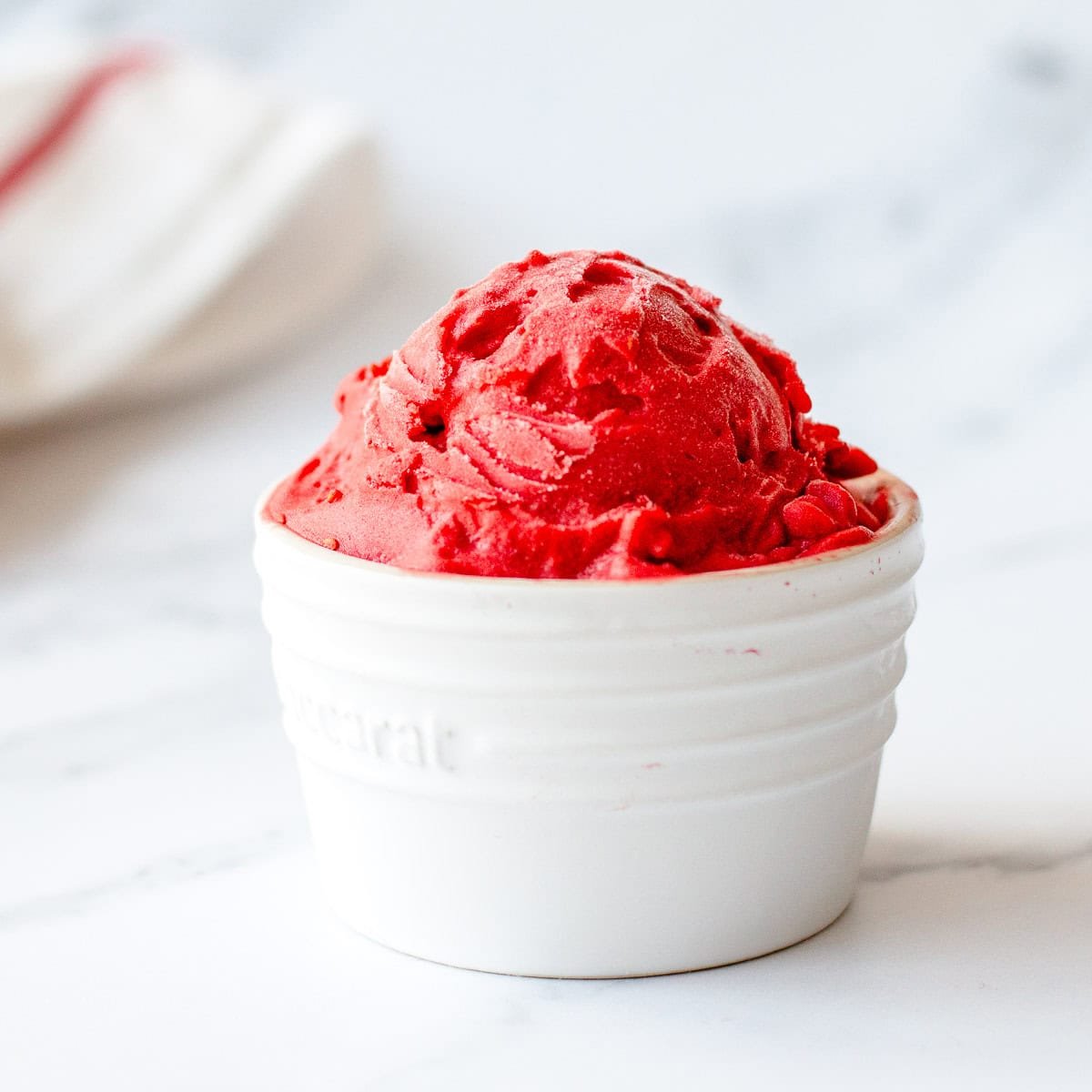 Raspberry sorbet in a cream ramekin on a white marble background.