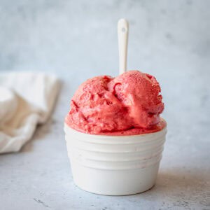 Raspberry Sorbet in a white ramekin with white spoon on a grey background.