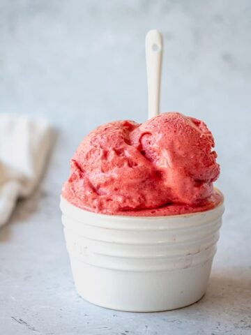 Raspberry Sorbet in a white ramekin with white spoon on a grey background.