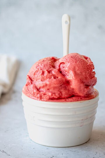 Raspberry Sorbet in a white ramekin with white spoon on a grey background.