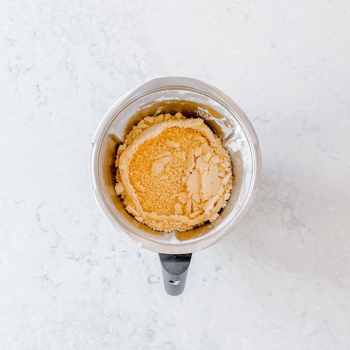 A silver mixing bowl filled with shortbread mixture sitting on a light marble countertop.