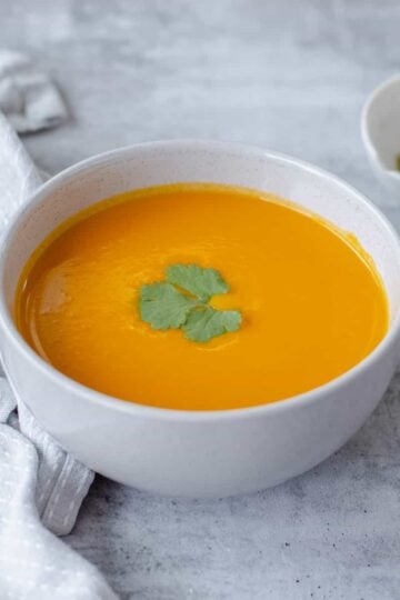 A close up image of Carrot & Coriander Soup in a grey bowl.