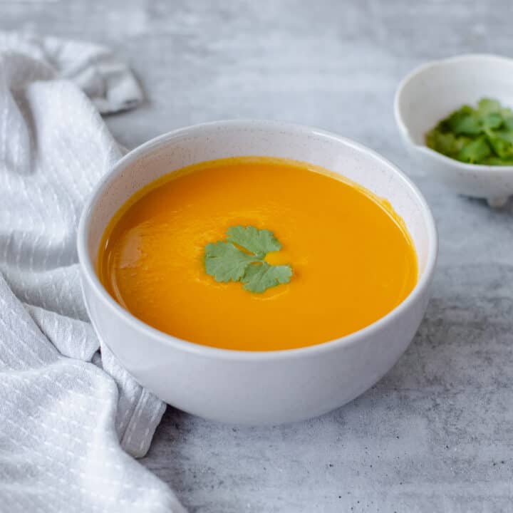 A close up image of Carrot & Coriander Soup in a grey bowl.