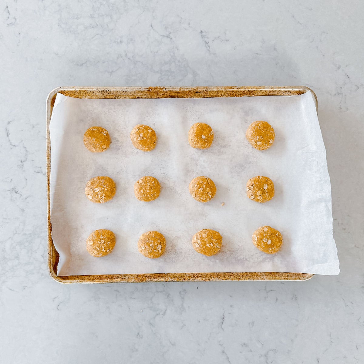 Raw anzac biscuits on a baking tray waiting to be baked.