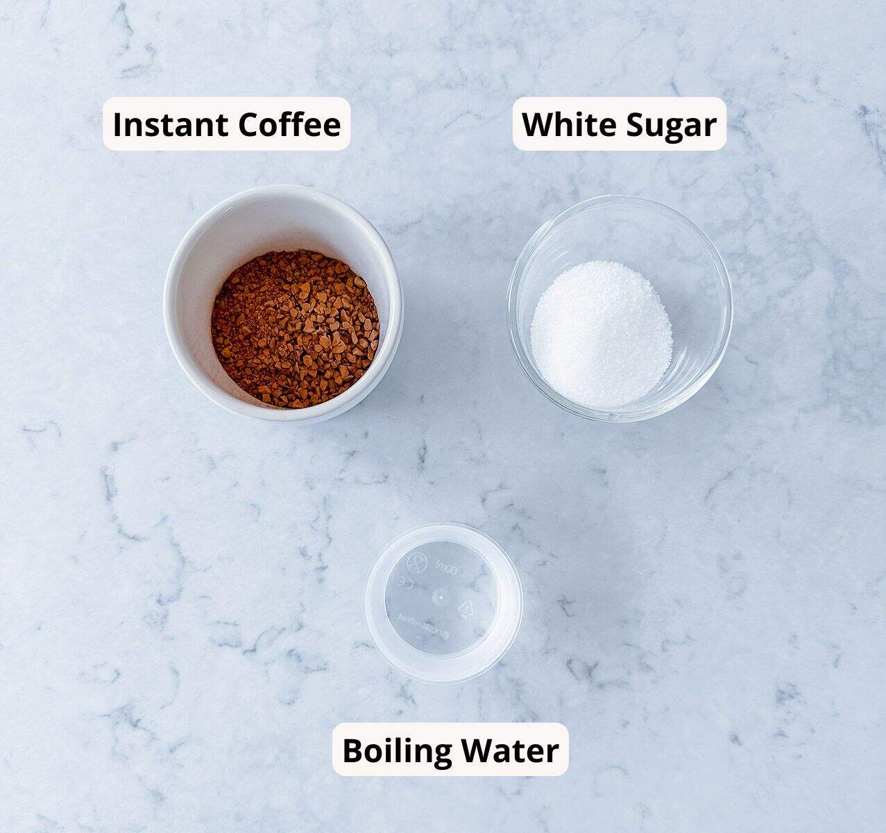 A bowl of instant coffee, a bowl of white sugar, and a cup of boiling water arranged on a marble surface, each labeled accordingly.