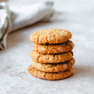 Anzac Biscuits stacked in a stack of 5, sitting on a marble benchtop