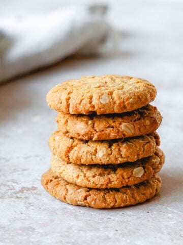 Anzac Biscuits stacked in a stack of 5, sitting on a marble benchtop