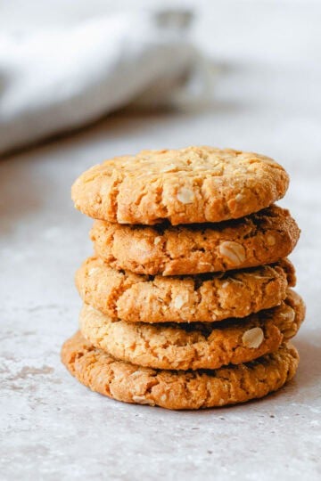Anzac Biscuits stacked in a stack of 5, sitting on a marble benchtop