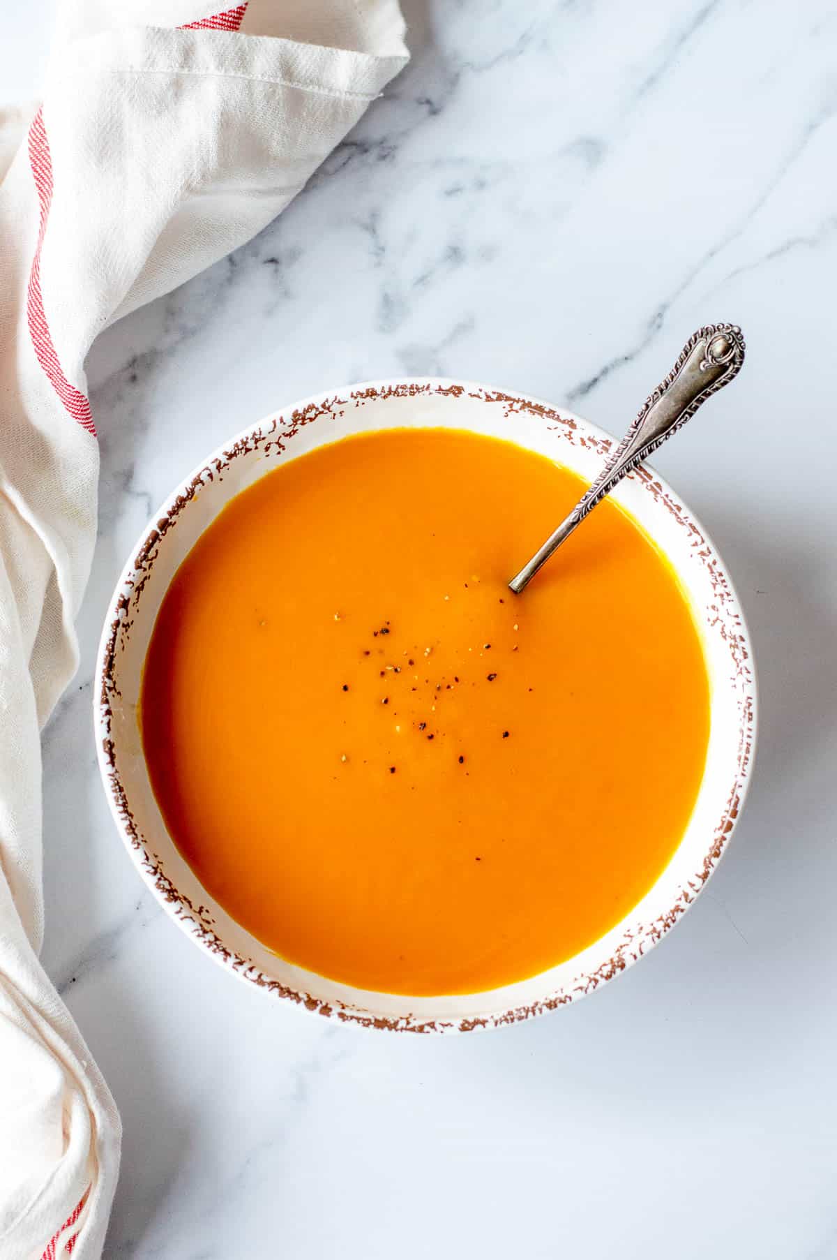 Pumpkin Soup in a white bowl sitting on a marble benchtop.