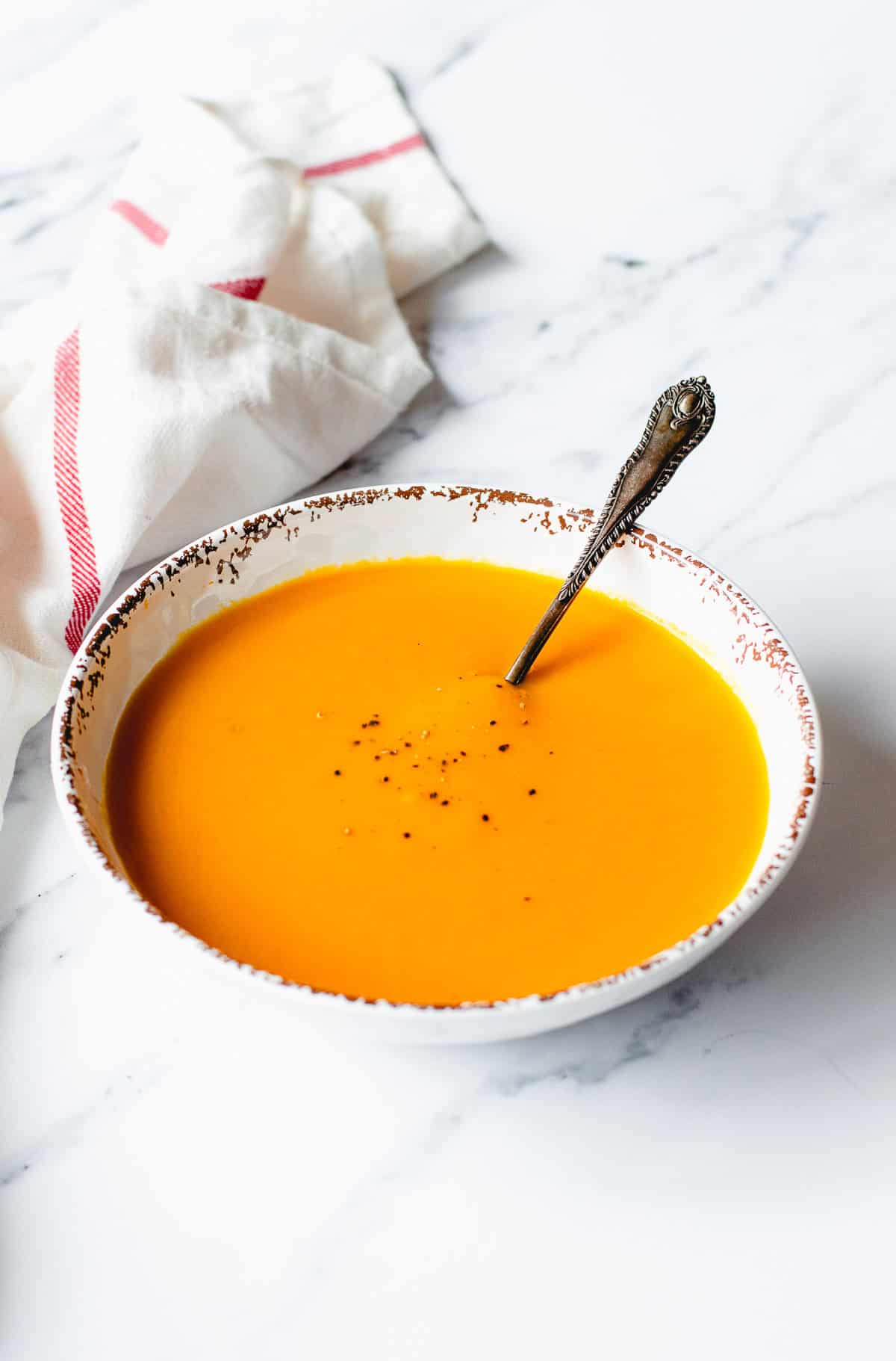 Pumpkin soup in a white bowl on a marble benchtop.