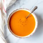 Pumpkin soup in a white bowl sitting on a marble background.