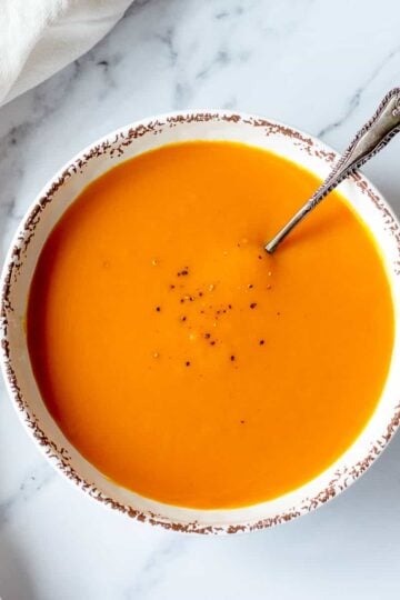 Pumpkin soup in a white bowl sitting on a marble background.