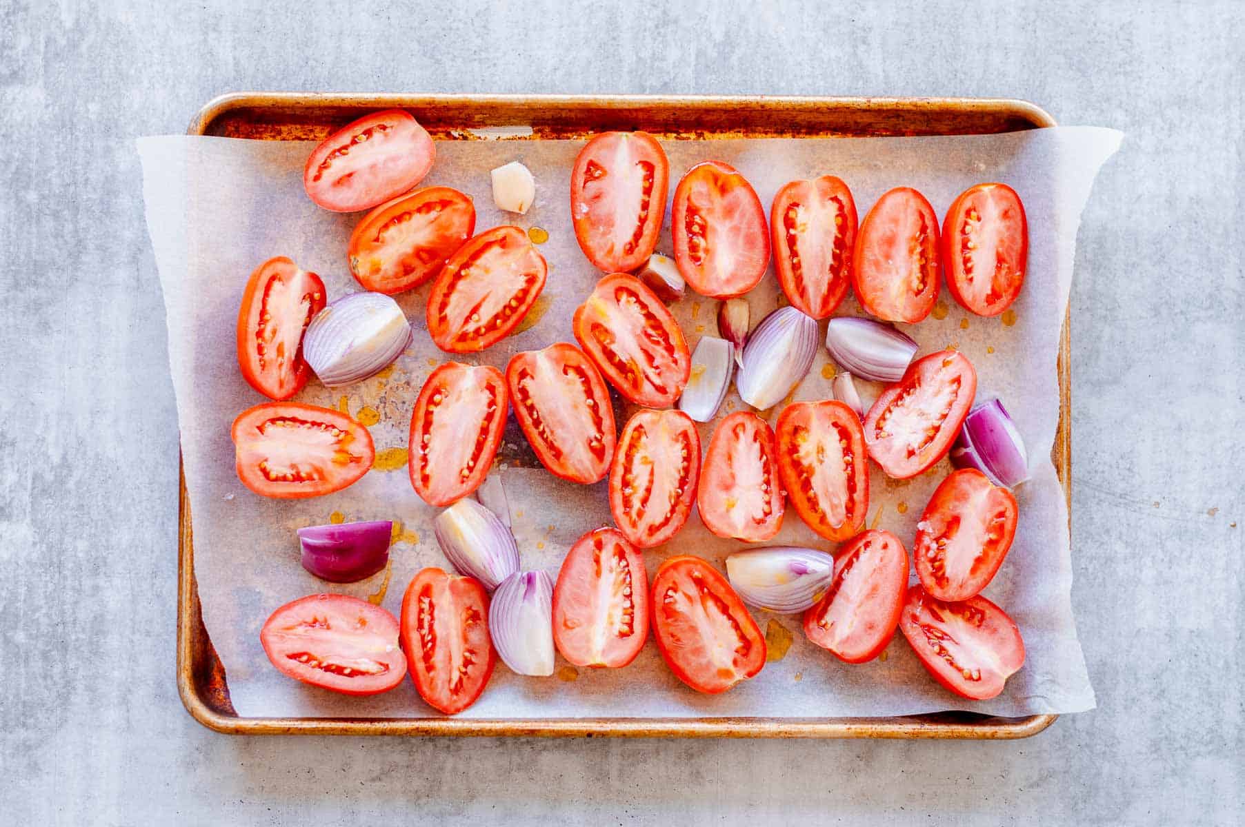 Tomatoes, red onion and garlic on a baking tray.