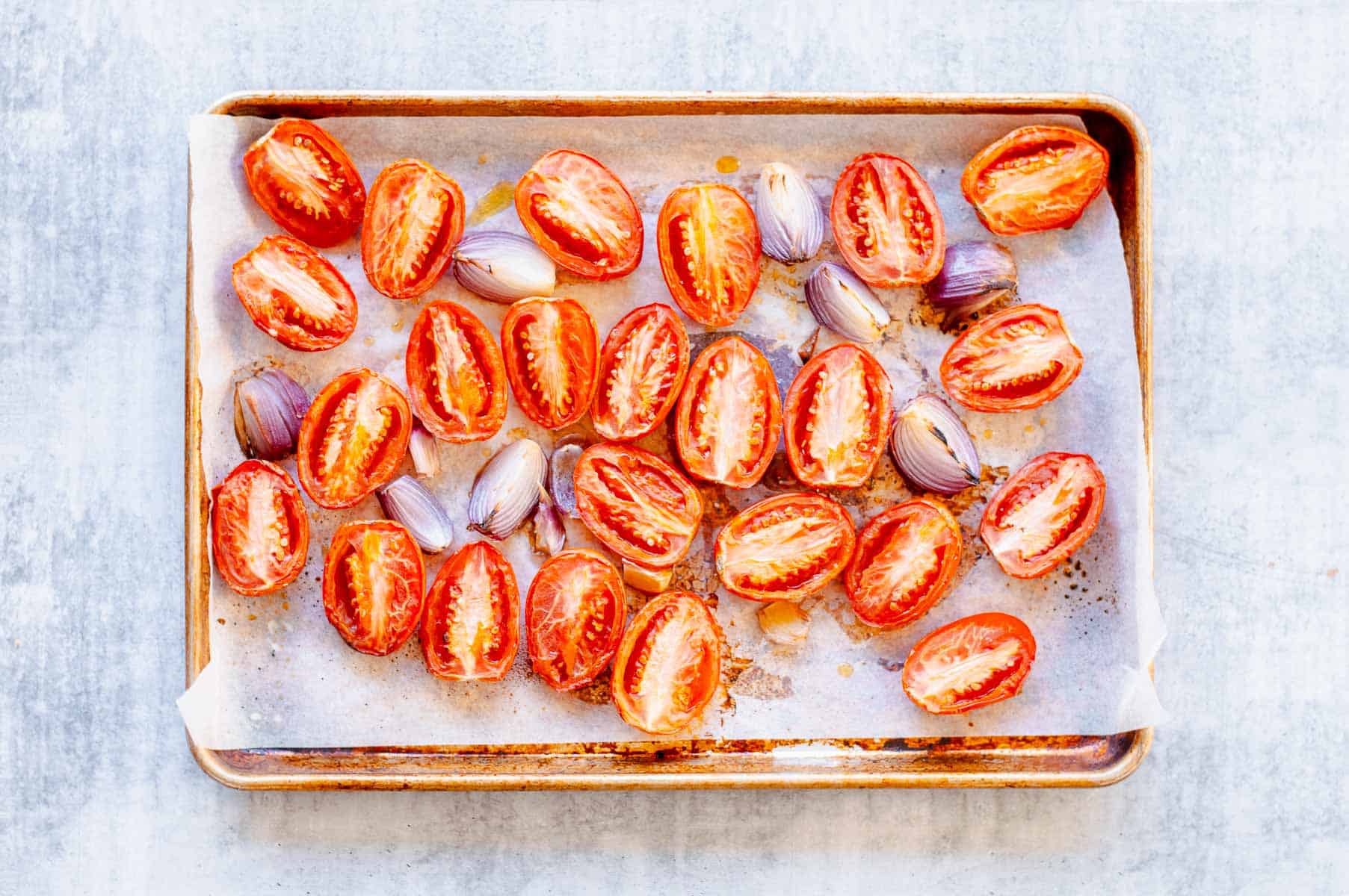 Roasted tomatoes, red onion and garlic on a baking tray.