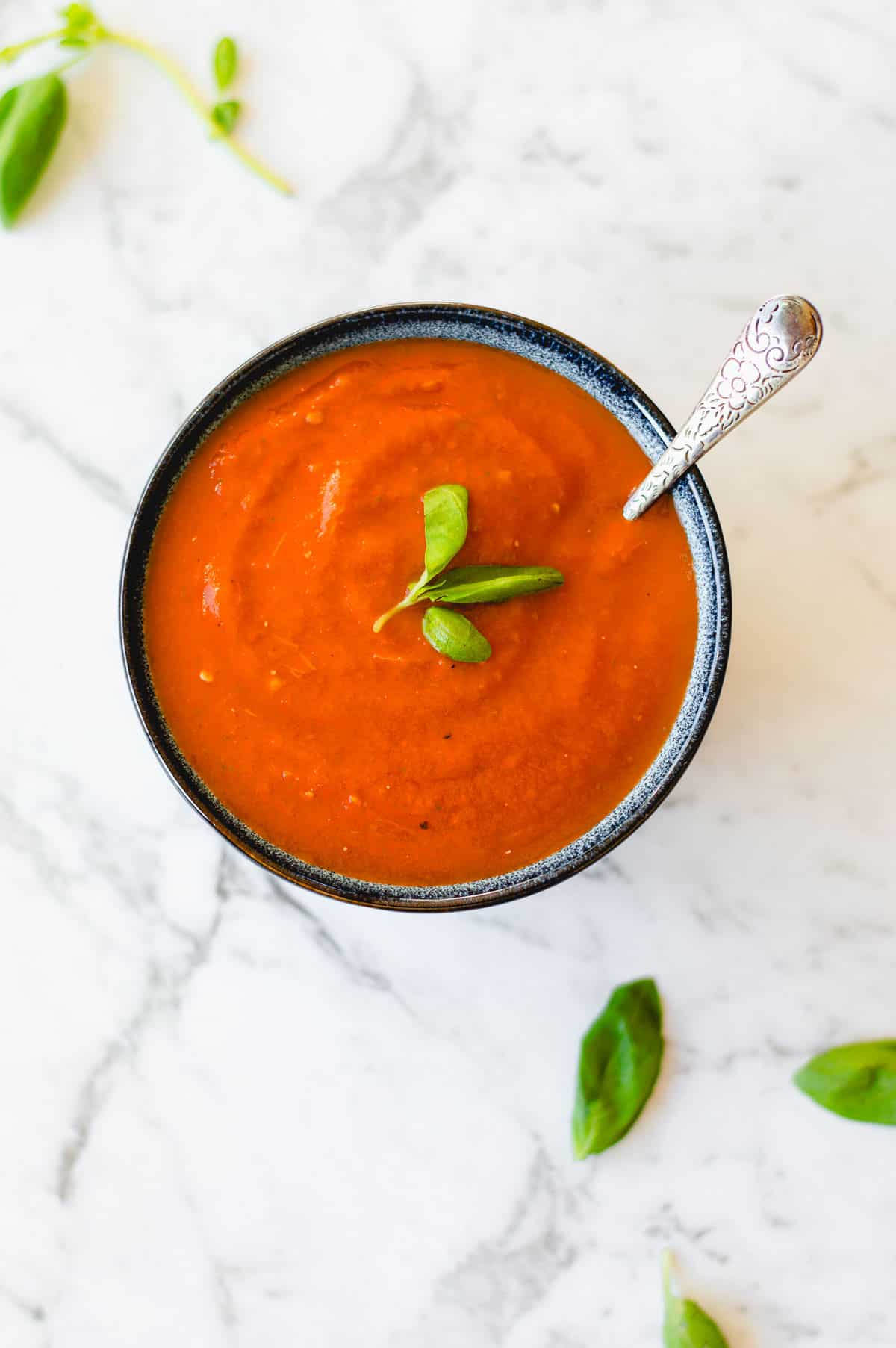 Tomato soup garnished with basil in a blue bowl.